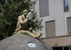 Magdeburg Statue eines Mannes mit Uhr auf Kugel vor modernem Gebäude