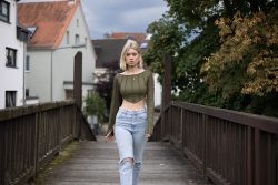 Portraitfotografie Available Light Frau auf Holzbrücke in Freizeitkleidung, umgeben von Häusern und Bäumen