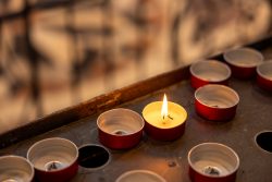 Venedig Entschleunigte Fotografie Oktober 2024 Eine brennende Kerze umgeben von unbeleuchteten Teelichtern in einem Metallgestell