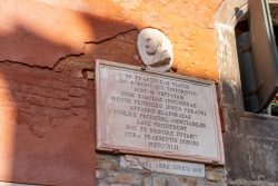 Venedig Entschleunigte Fotografie Oktober 2024 Gedenktafel an roter Backsteinwand mit lateinischer Inschrift und Marmorbüste