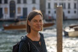 Venedig Entschleunigte Fotografie Oktober 2024 Frau lächelt am Ufer eines Kanals, während Boote im Hintergrund vorbeifahren