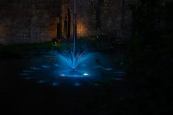 Bad Vilbel Herbst 2022 Fotoserie Aloys Peter Trenz Blauer Wasserbrunnen beleuchtet in nächtlicher Umgebung mit Skulpturen im Hintergrund