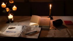 Fotografie Stillleben Aloys Peter Trenz Beleuchteter Schreibtisch mit Kerzen, Buch und Notizblock
