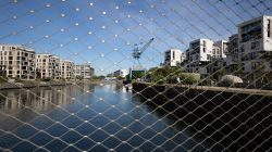 Brücken am Main - Fotoserie Aloys Peter Trenz Moderne Wohngebäude am Flussufer hinter Sicherheitszaun