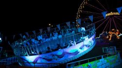 Fotografie Experimente mit Licht und Bewegung August 2022 Nachtaufnahme eines beleuchteten Karussells auf einem Jahrmarkt mit Riesenrad im Hintergrund