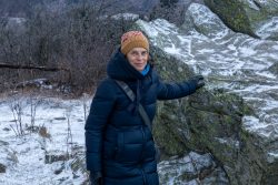 Landschaftsfotografie Großer Feldberg Taunus Winter Januar 2025 Frau in Winterkleidung neben schneebedecktem Felsen in winterlicher Landschaft