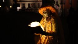 Halla Venezia Schwäbisch Hall Februar 2023 Eine maskierte Figur in Venedig, die nachts ein leuchtendes Buch liest Halla Venezia Schwäbisch Hall Februar 2023 Person in St. Mark's Square in glanzvoller venezianischer Maske liest ein beleuchtetes Buch