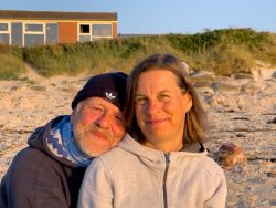 Helgoland Ein lächelndes Paar sitzt im Abendlicht am Strand. Helgoland Paar lächelt am Strand vor Dünen und Gebäude