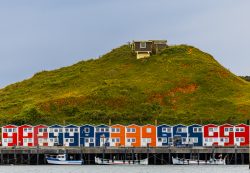 Helgolandreise August 2023 Bunte Hütten reihen sich vor einem grünen Hügel an der Küste auf. Helgolandreise August 2023 Bunte Strandhütten vor grasbewachsenem Hügel mit blauem Himmel