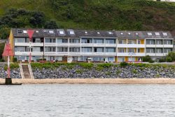 Helgolandreise August 2023 Apartmentgebäude an einer ruhigen Küste, umgeben von grüner Natur. Helgolandreise August 2023 Strandpromenade mit Apartmentgebäuden und grüner Hügelkulisse