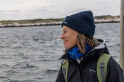 Helgolandreise August 2023 Eine Frau auf einer Bootsfahrt im Winter trägt eine warme Mütze und Jacke Helgolandreise August 2023 Frau genießt eine Bootsfahrt auf einem See mit Mütze und Winterjacke