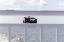 Helgolandreise August 2023 Ein großes Frachtschiff bewegt sich über den weiten Ozean Helgolandreise August 2023 Frachtschiff auf offener See hinter Geländer fotografiert