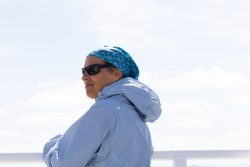 Helgolandreise August 2023 Eine Frau genießt die Aussicht von einem Schiff an einem klaren Tag Helgolandreise August 2023 Frau in blauer Jacke und Sonnenbrille auf einem Schiff vor hellem Himmel