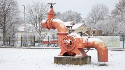 Landschaftsfotografie Winter Gernsheim Dezember 2022 Ein altes, rotes Industrieventil steht auf einem verschneiten Platz. Landschaftsfotografie Winter Gernsheim Dezember 2022 Großes Industrieventil im verschneiten Außenbereich
