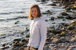 Portraitfotografie Fotoshooting Strand Helgoland August 2024 Frau in grauer Jacke am felsigen Strand bei Sonnenuntergang am Meer