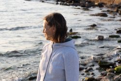 Portraitfotografie Fotoshooting Strand Helgoland August 2024 Frau am felsigen Strand blickt auf das Meer bei Sonnenuntergang