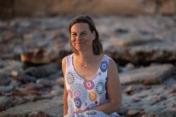 Portraitfotografie Fotoshooting Strand Helgoland August 2024 Frau in gemustertem Kleid sitzt auf Felsen am Strand bei Sonnenuntergang