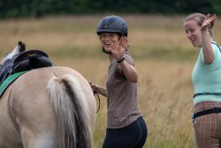 Reitstunde Fotografie Aloys Peter Trenz Zwei Frauen winken und führen ein Pferd auf einem Feld