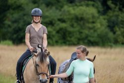 Reitstunde Fotografie Aloys Peter Trenz Frau reitet ein Pferd auf einer Wiese mit Begleiter