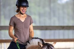 Reitstunde Fotografie Aloys Peter Trenz Eine Frau reitet lächelnd auf einem Pferd in einer Reithalle