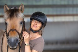 Reitstunde Fotografie Aloys Peter Trenz Frau in Reithelm steht mit Pferd in Halle