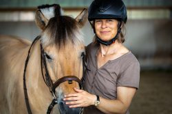 Reitstunde Fotografie Aloys Peter Trenz Frau mit Helm und lächelnden Gesicht streichelt ein Pferd in einer Reithalle
