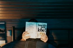 Storytelling Sorge Dich nicht lebe - The Day after Person liest Buch 'Sorge dich nicht - lebe' im Bett unter gedämpftem Licht