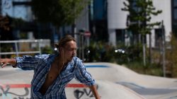 Urban Life und Streetfotografie Frankfurt Juni 2022 Mann fährt Skateboard im Park, Wind im offenen Hemd, Stadtkulisse im Hintergrund