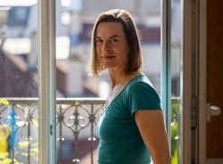 Paris Juni 2026 Frau in blauem Oberteil steht lächelnd vor einem offenen Fenster