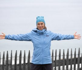 Saint-Malo Oktober 2026 Frau in blauem Anorak und Mütze steht lächelnd mit ausgestreckten Armen am Meer